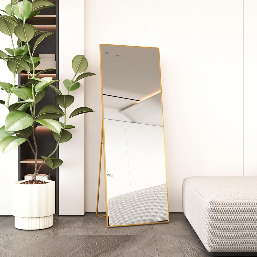 A full-length mirror with a gold frame, standing in a modern living room setting, with a free-standing design and a gold metal bracket.