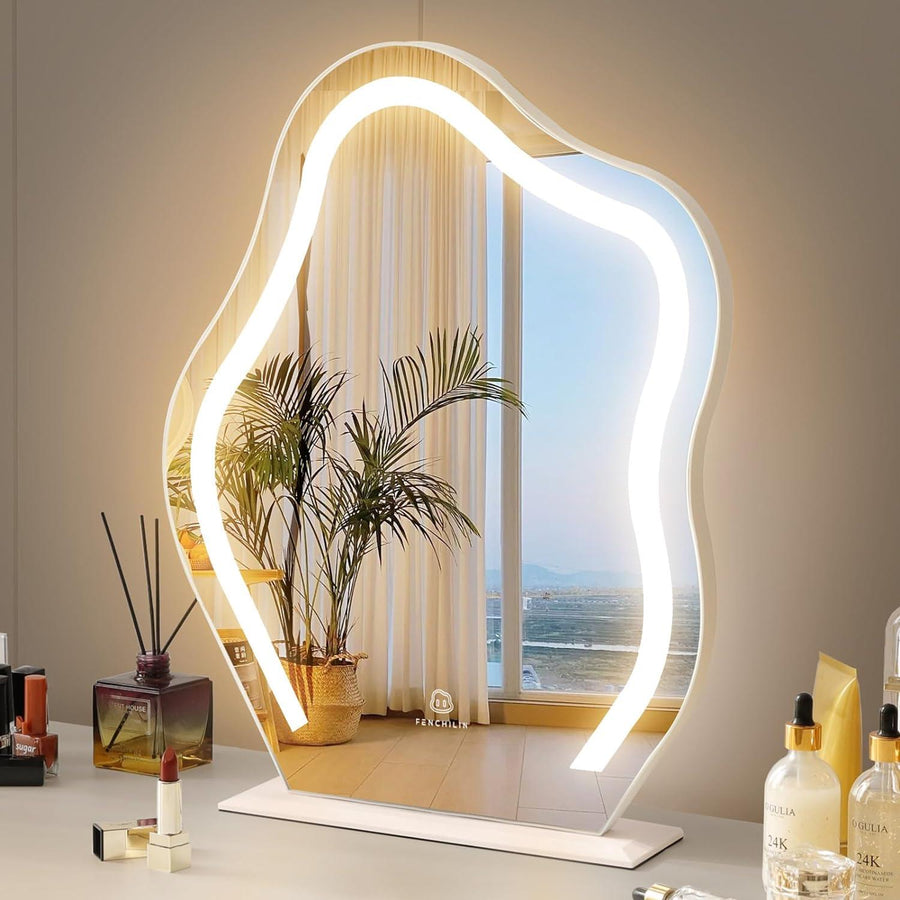 An irregularly shaped vanity makeup mirror with lights, placed on a table with items around it, reflecting light and an indoor plant in the background.
