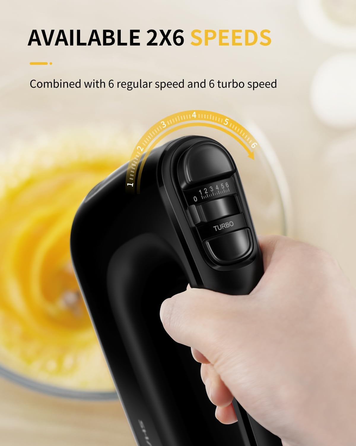 Handheld mixer with speed control dial held by a hand, blurred background of a bowl with yellow mixture.