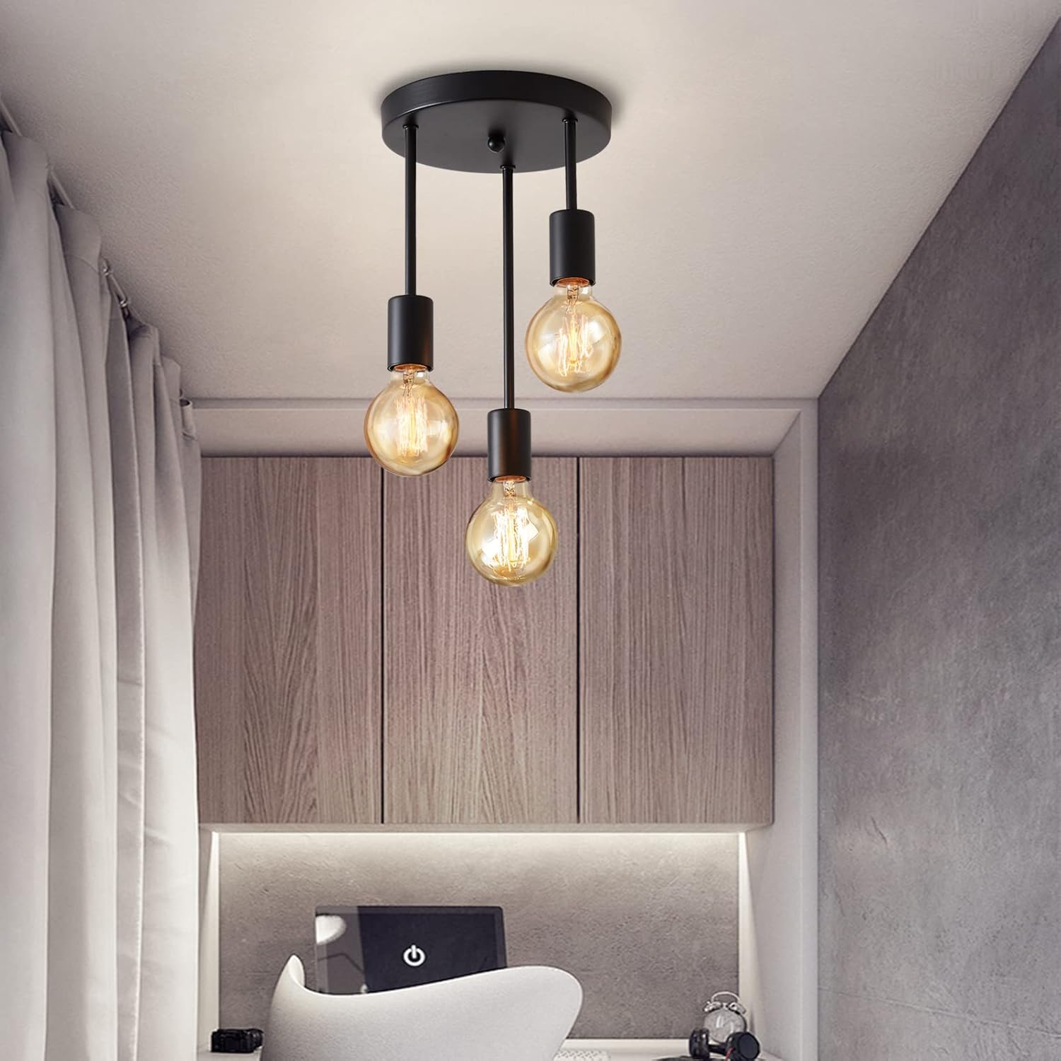 Modern ceiling light fixture with three exposed bulbs in a room with wooden cabinets and a chair.