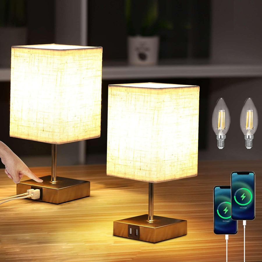 Two table lamps with a hand plugging in a device, two light bulbs, and two smartphones on a wooden surface.