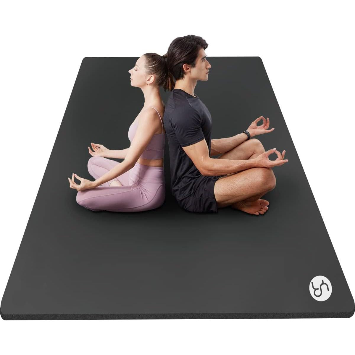 Two people sitting on a black yoga mat with a visible brand logo.