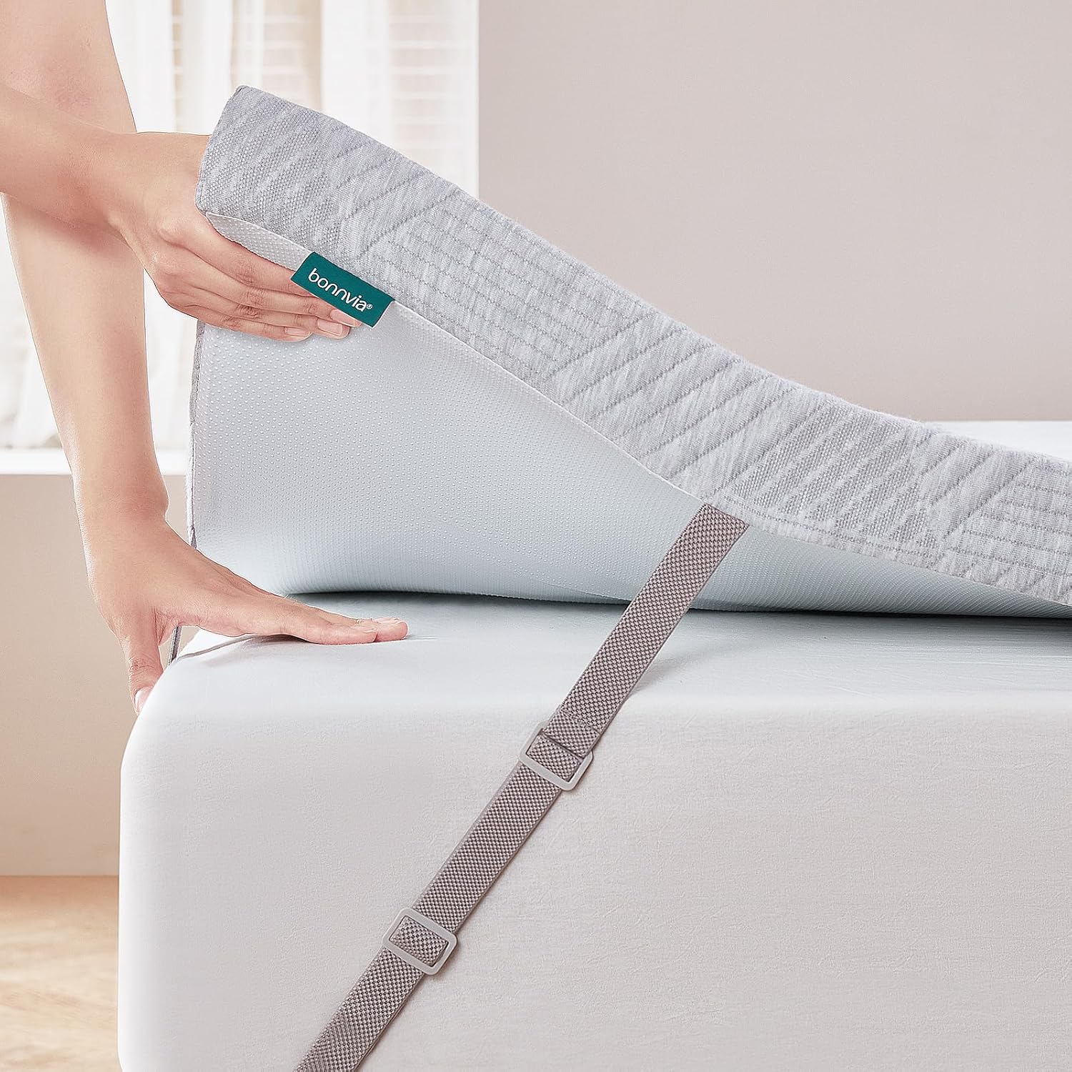 Person adjusting a fitted sheet on a bed with a Bonmaté label.