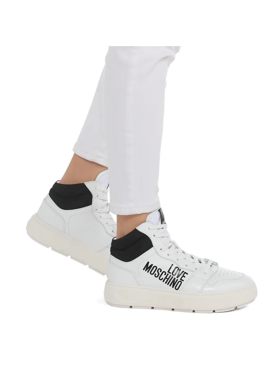 White sneakers with 'Love Moschino' branding worn with white pants on a white background