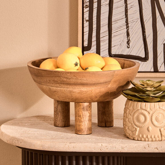 Wooden bowl with fruits on a table next to a plant