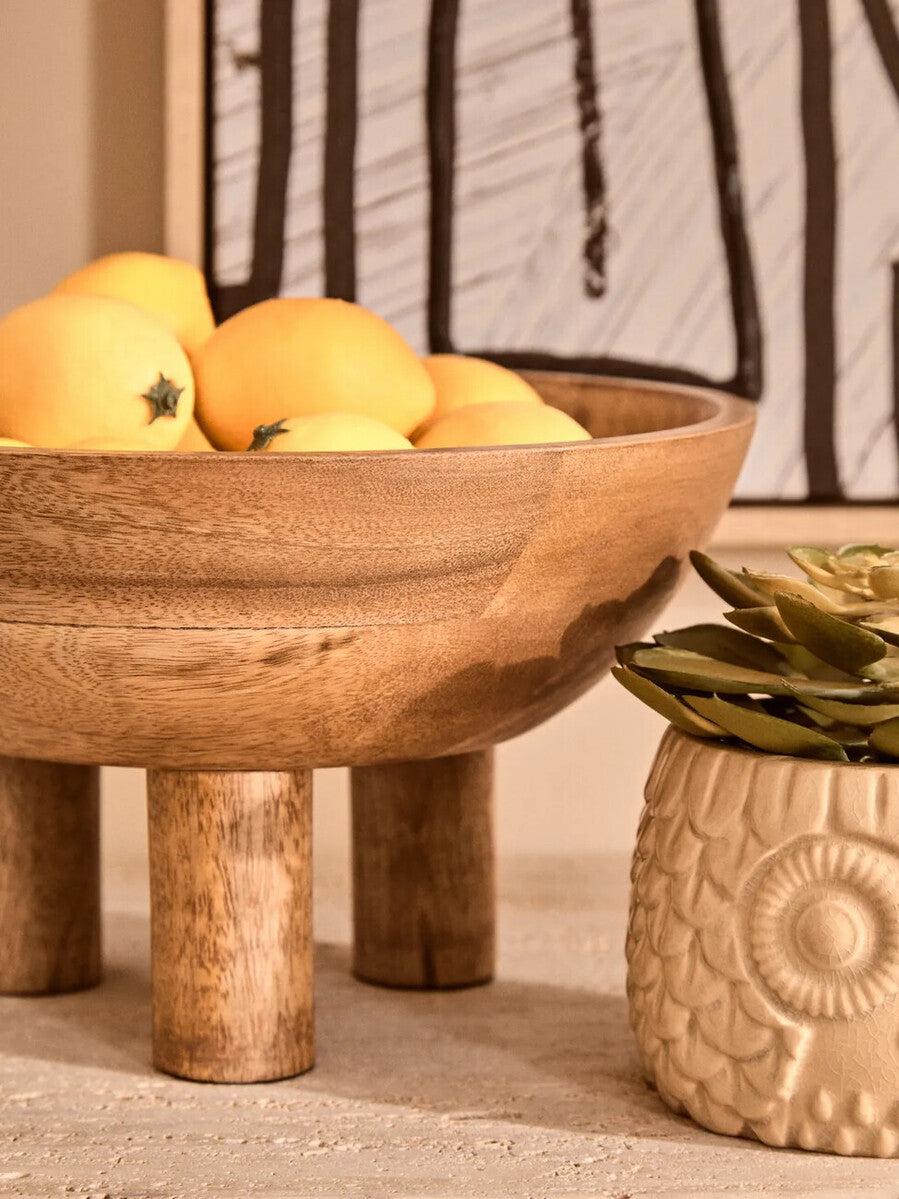 Wooden bowl with fruits on a textured surface next to a decorative pot.
