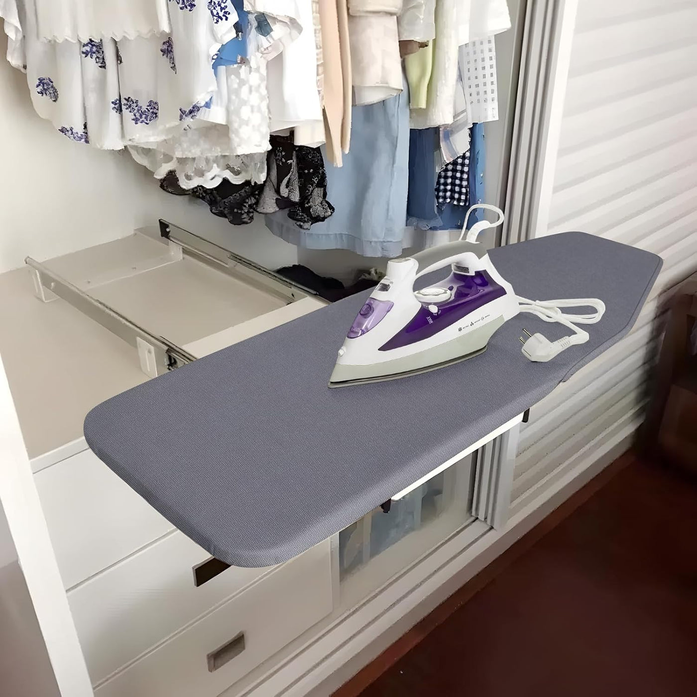 Ironing board with an iron on top, next to a closet with hanging clothes.