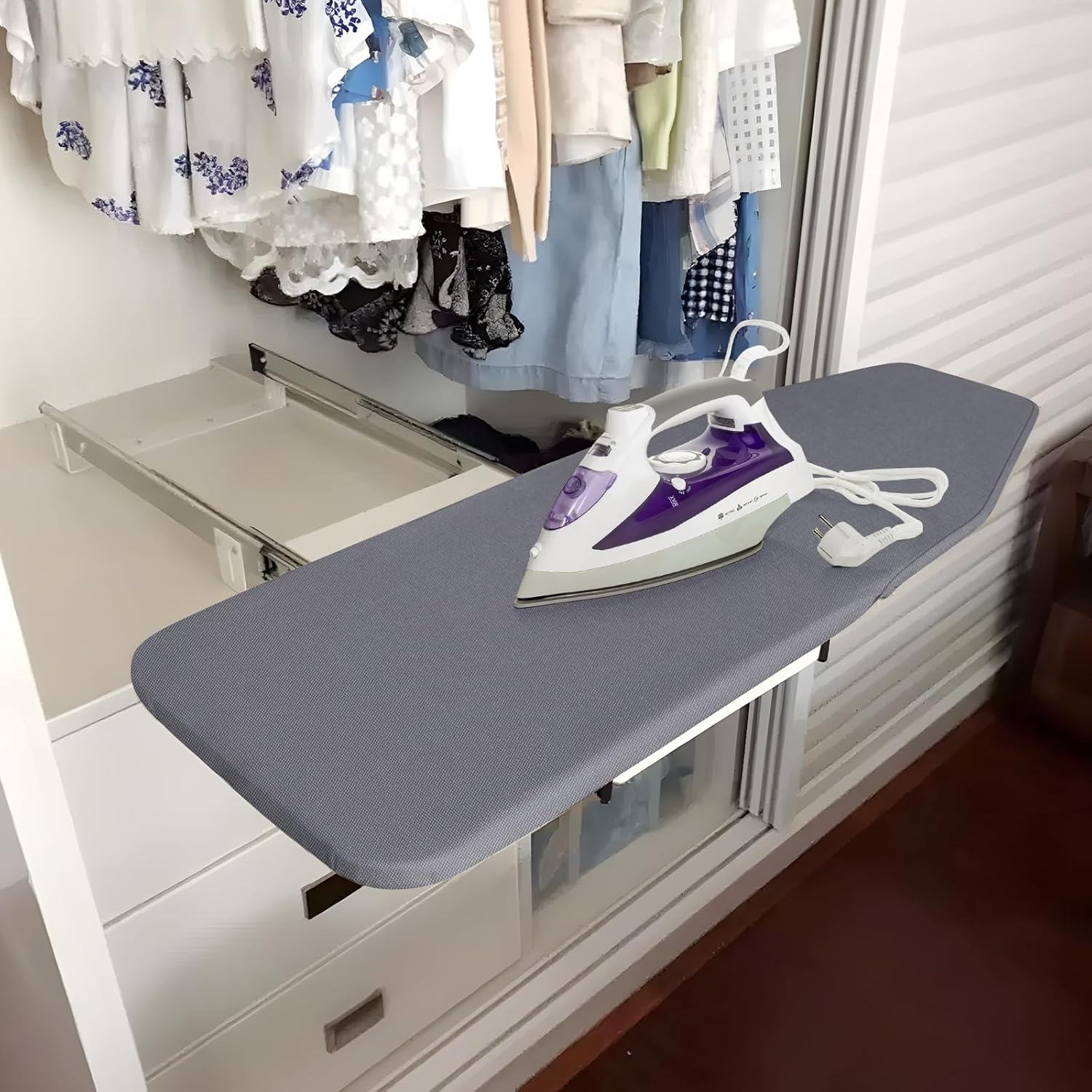 Ironing board with an iron on top, next to a closet with hanging clothes.
