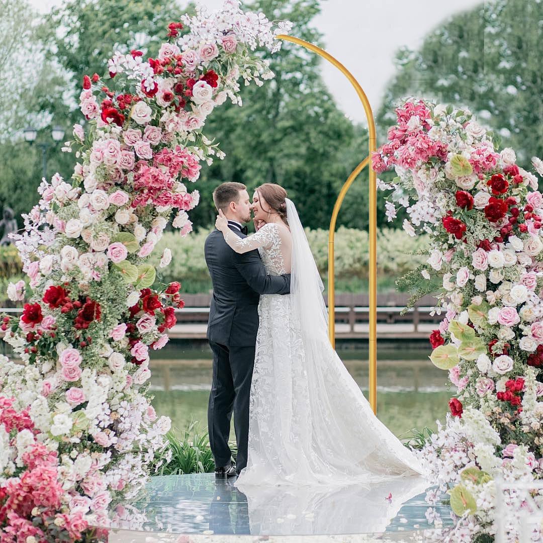 Couple kissing under a floral arch with a lake and trees in the background