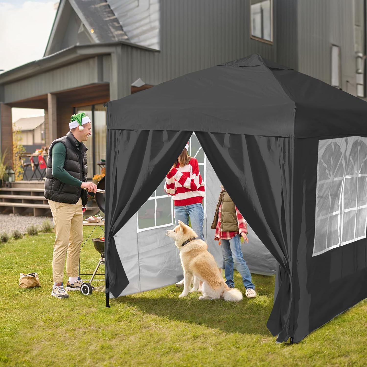 Black pop-up canopy tent with curtains set up outdoors, people and a dog nearby.
