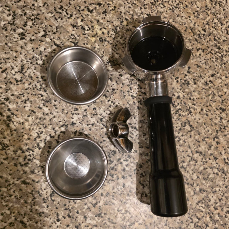 Coffee brewing components including a black handle and metal parts on a granite countertop.