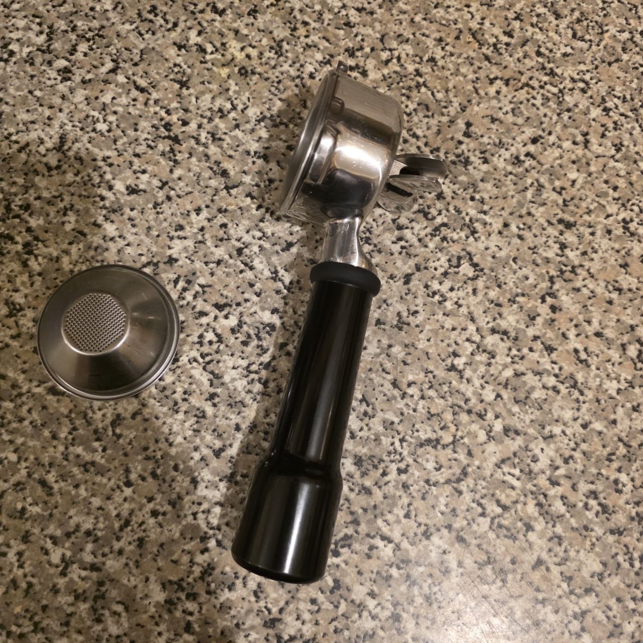 Coffee grinder with black handle and metal parts on a speckled countertop