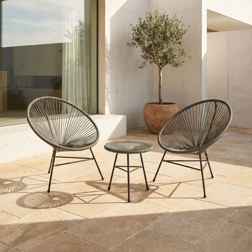 Two outdoor chairs and a small table on a stone patio with a plant in the background.