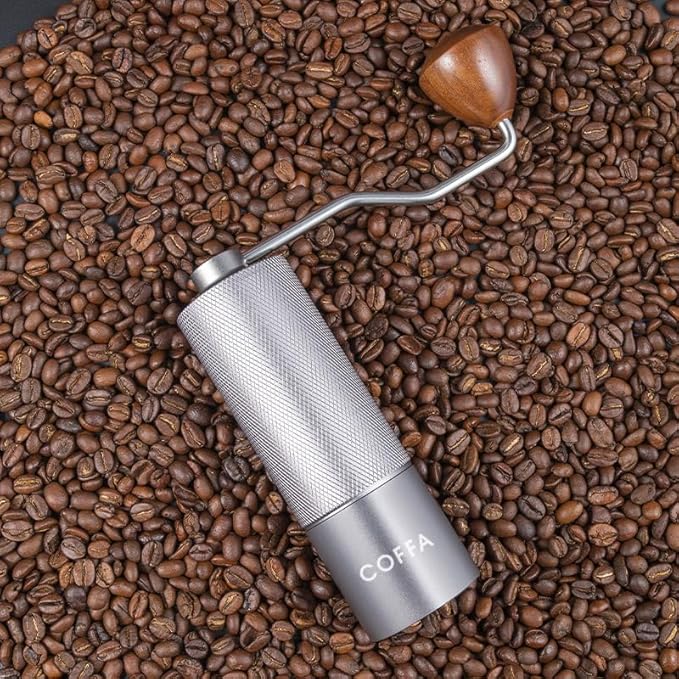 Handheld coffee grinder on a bed of coffee beans with 'COFFA' branding.