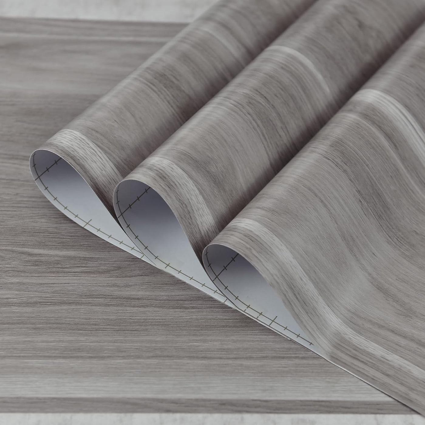 Rolls of gray wood-patterned vinyl flooring on a light gray background