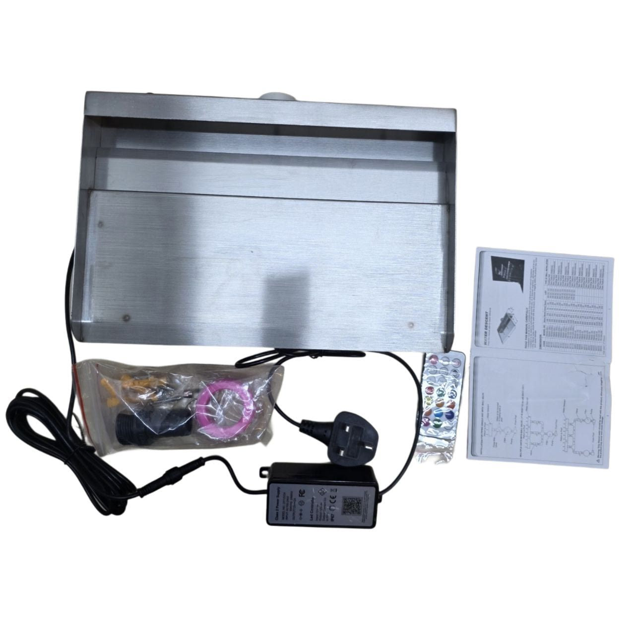 Metallic electronic device with cables, power adapter, and user manual on a white background