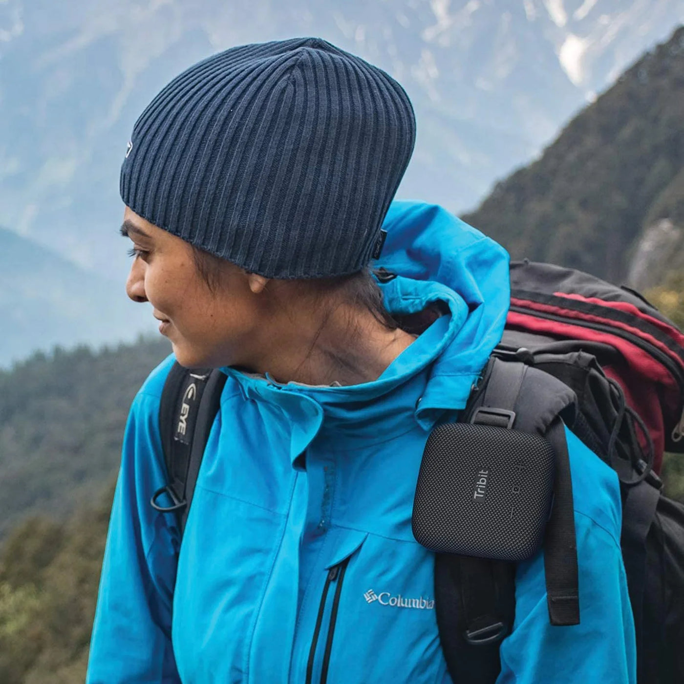 Person wearing a blue jacket and black beanie with a backpack in a mountainous area