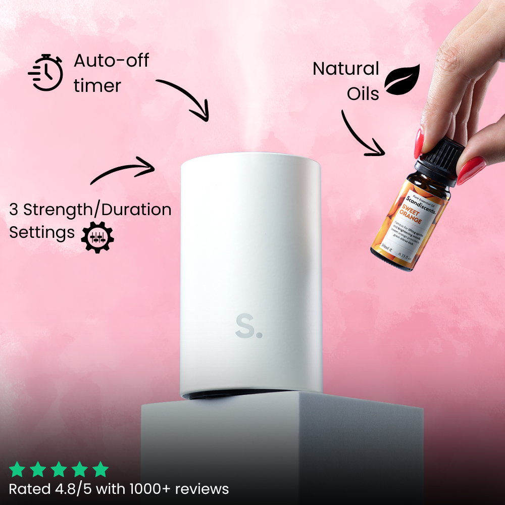 White diffuser with a hand holding a bottle of essential oils against a pink background