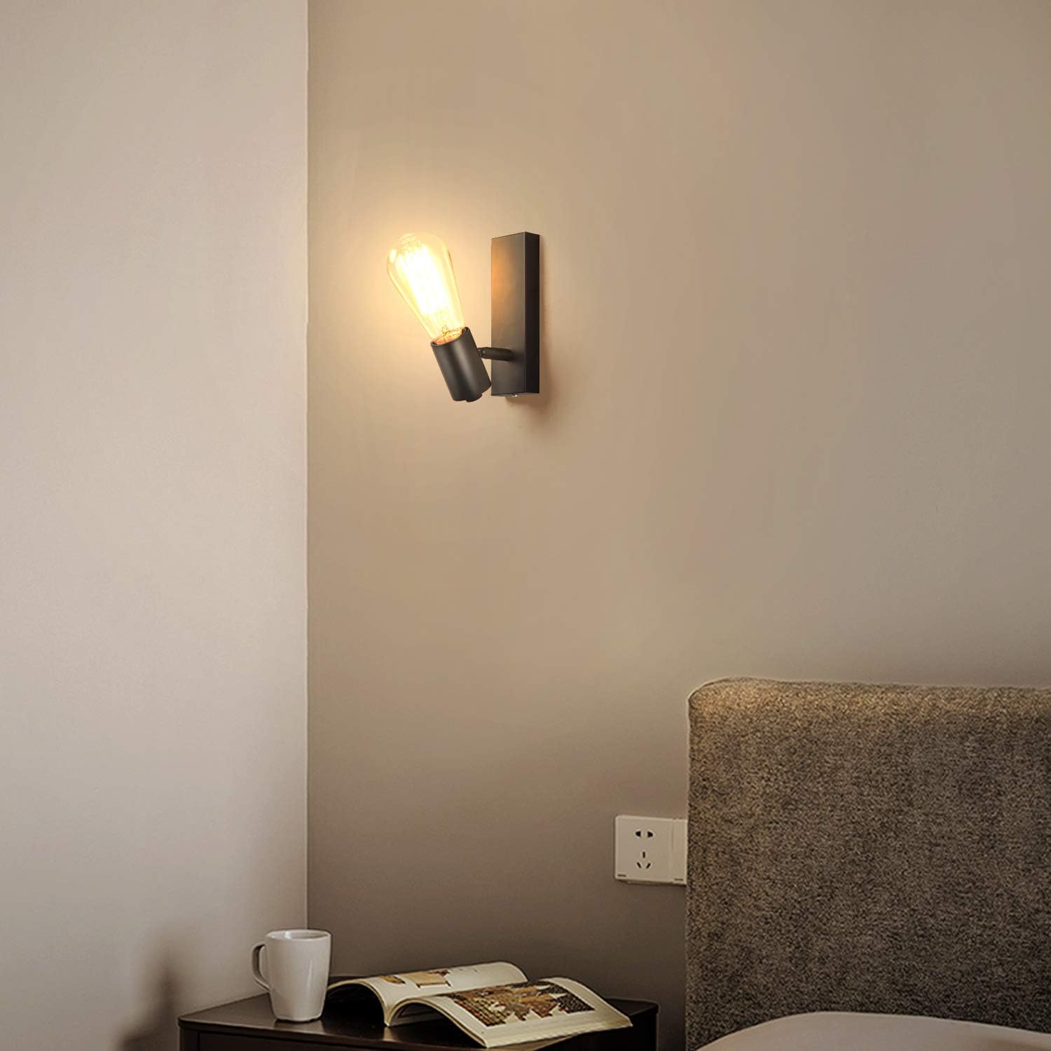 Wall-mounted light fixture on a beige wall next to a bed with a nightstand and open book.