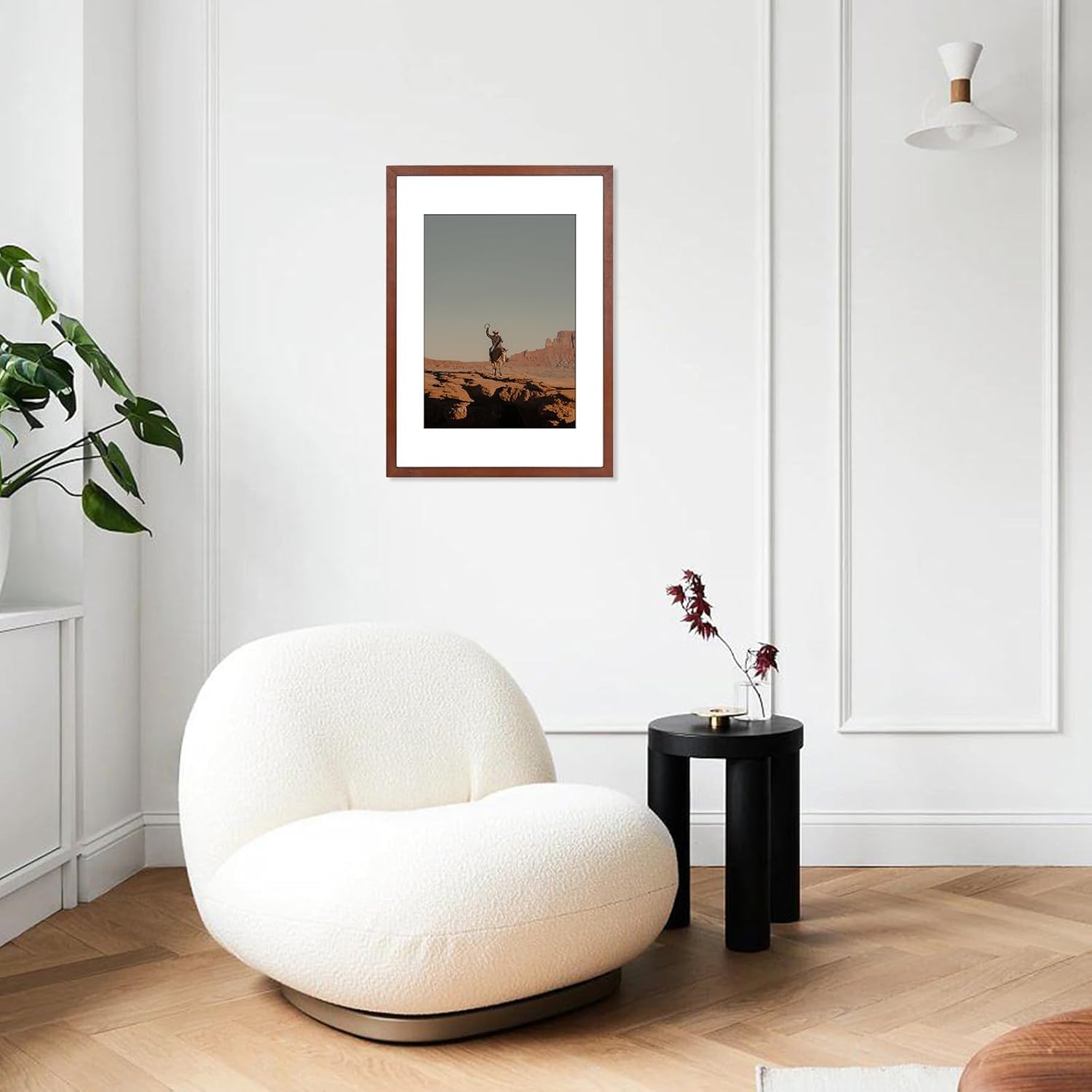 Modern living room with a white armchair, black side table, and framed artwork on a white wall.