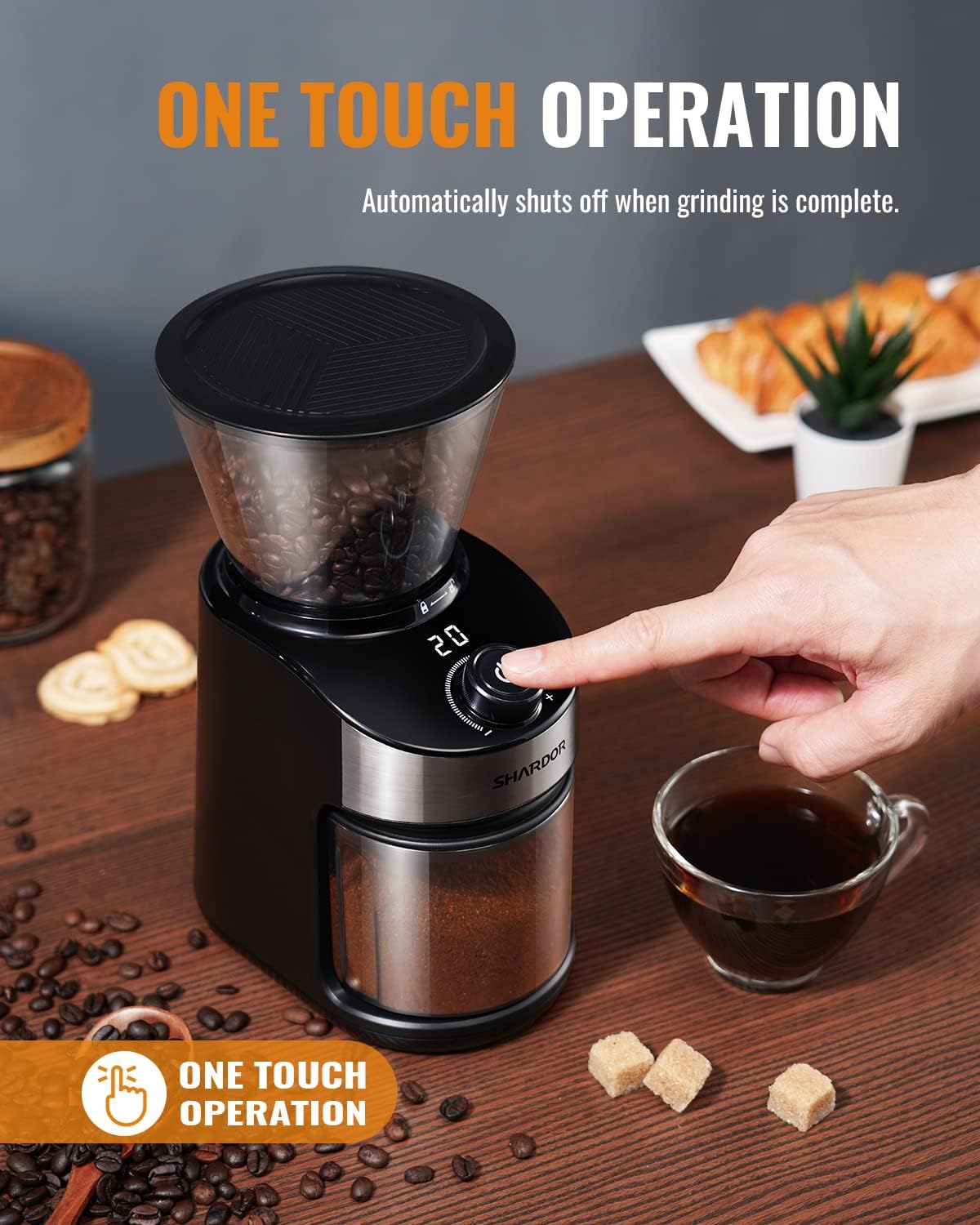 Coffee grinder with one touch operation feature on a table with coffee beans and a cup of coffee.
