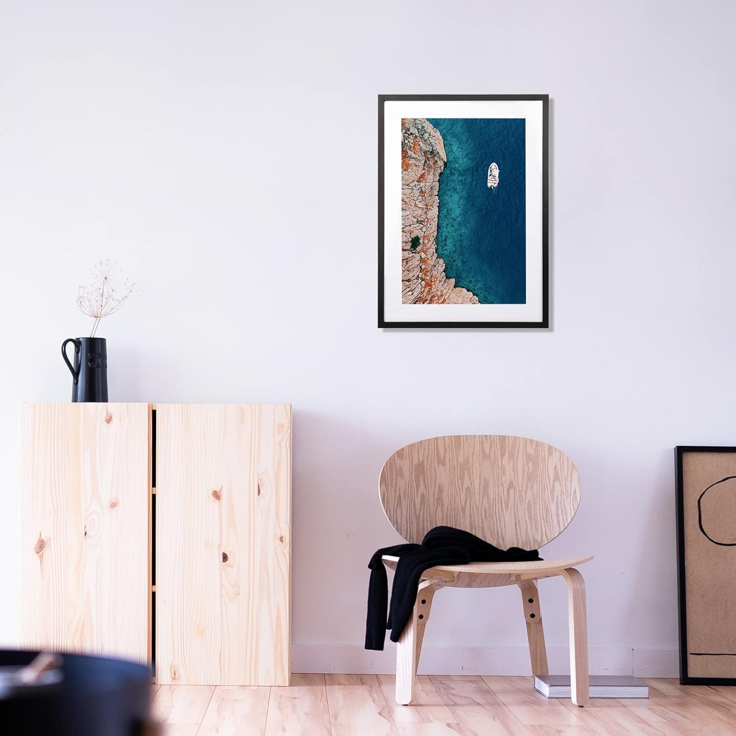 Framed artwork on a wall above a wooden chair in a room.