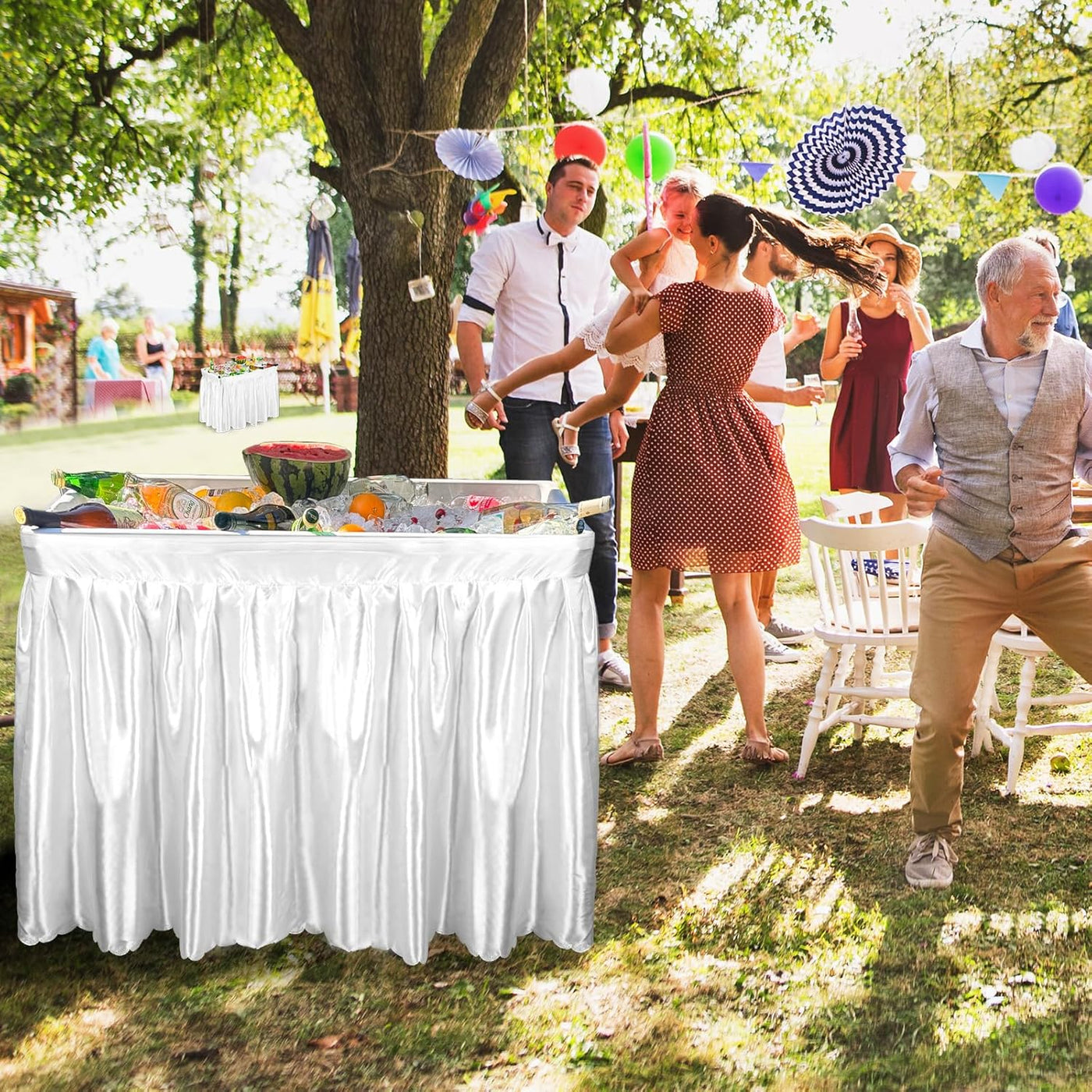 People socializing outdoors at a party with a decorated table and colorful balloons.