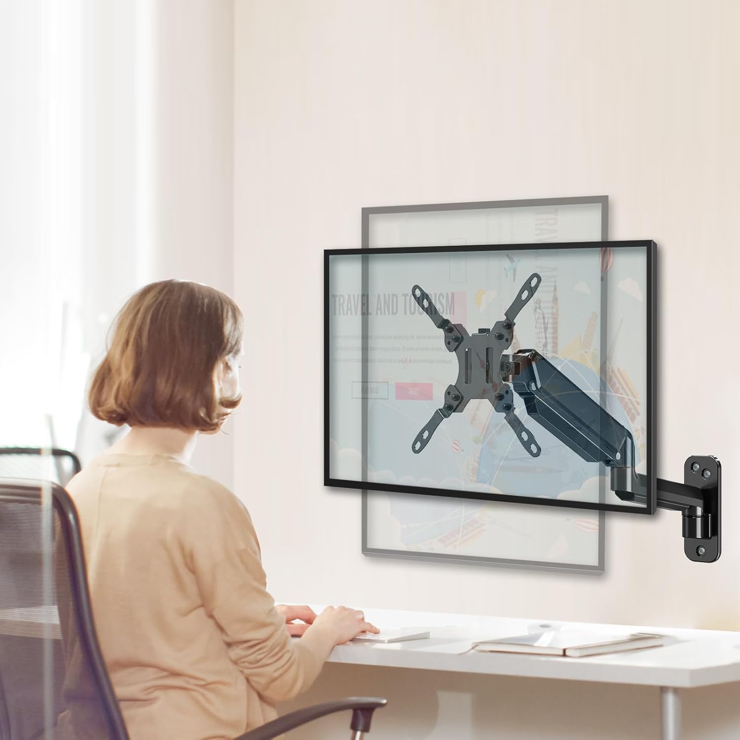 Person sitting at a desk using a computer with a monitor arm attached to the wall.