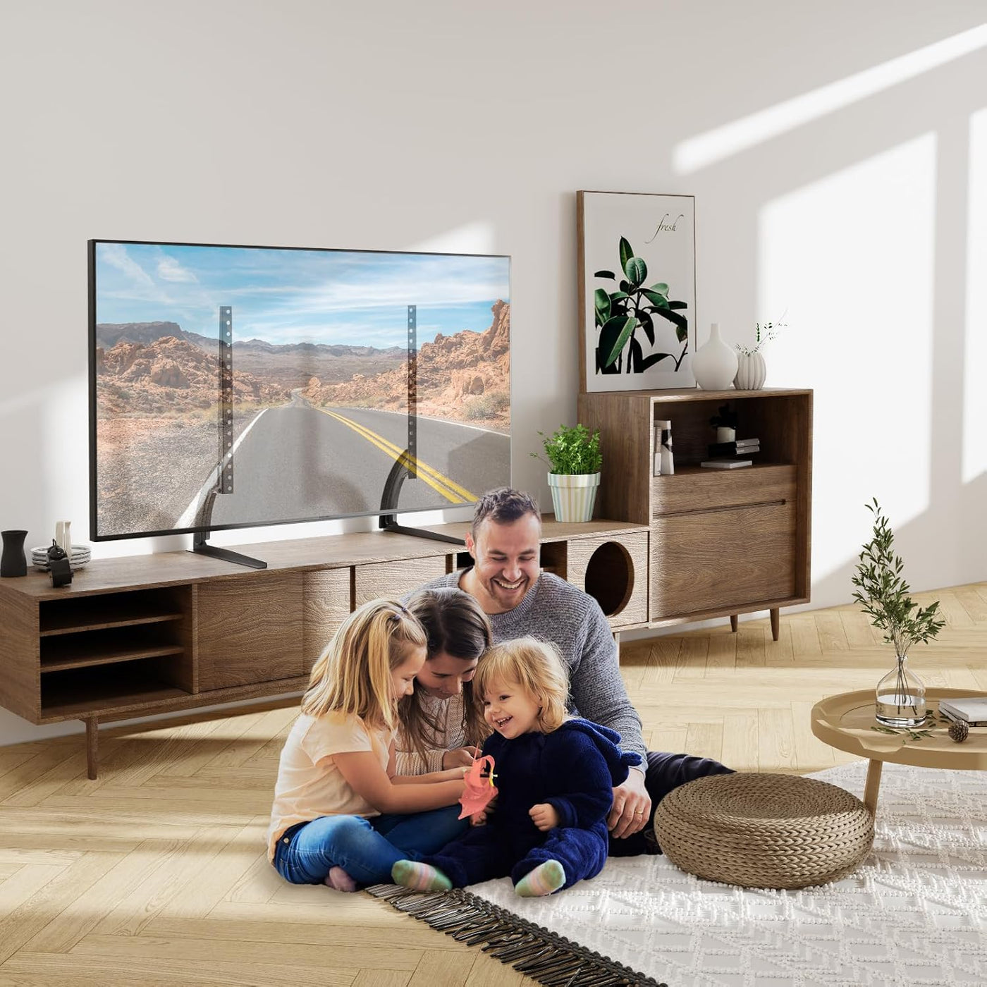 Family sitting on the floor in a modern living room with a large TV displaying a scenic road.