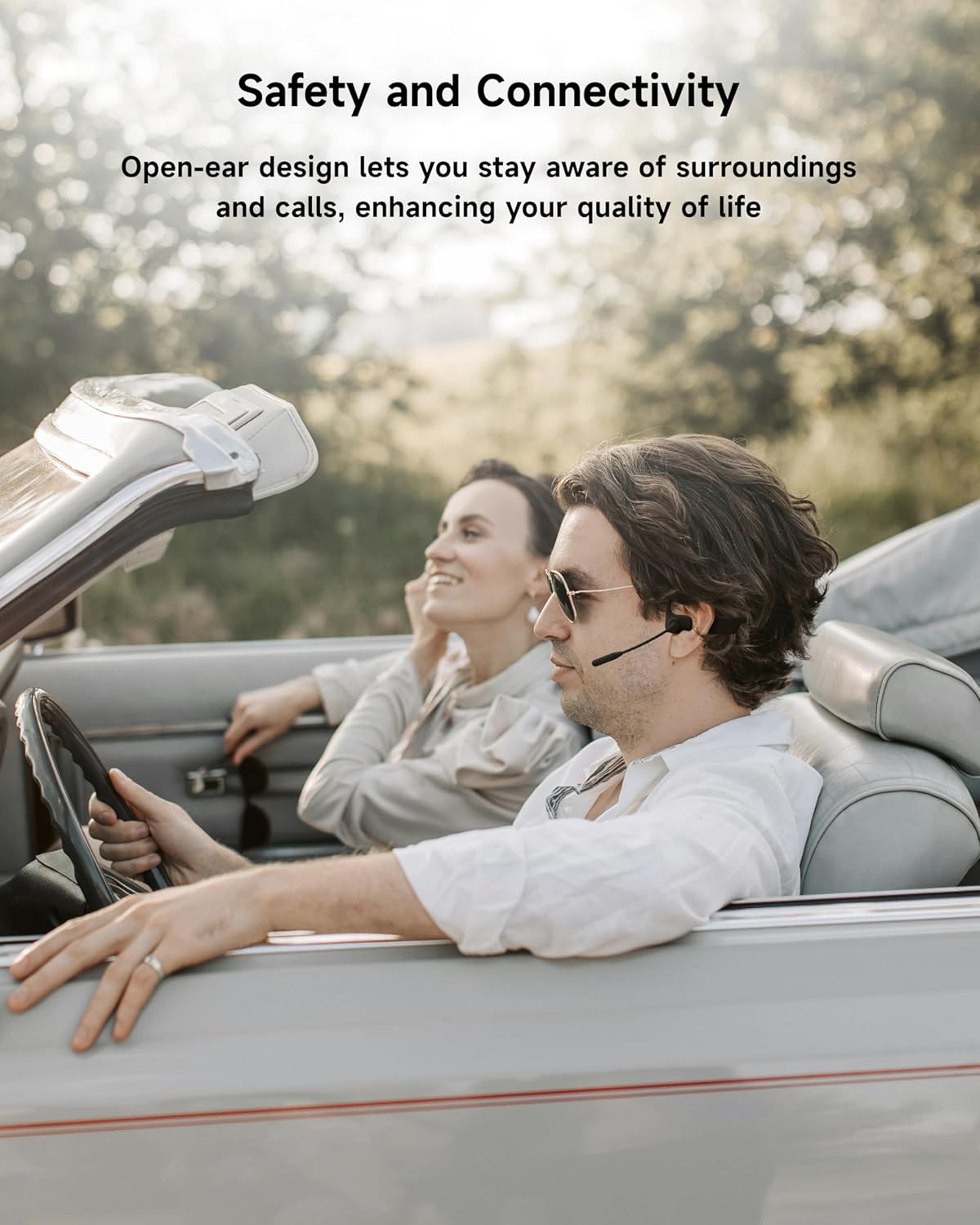 Man driving a convertible car with a woman in the passenger seat, wearing open-ear headphones.