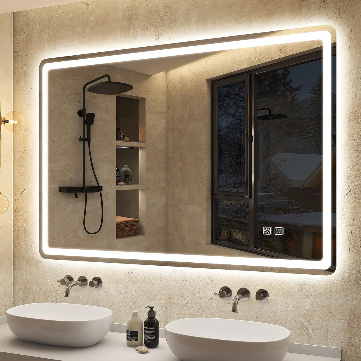 A large rectangular LED-backlit bathroom mirror mounted on a textured beige stone wall above a double-sink vanity. The mirror reflects a black shower fixture and a window view, with two white vessel sinks and chrome faucets below.