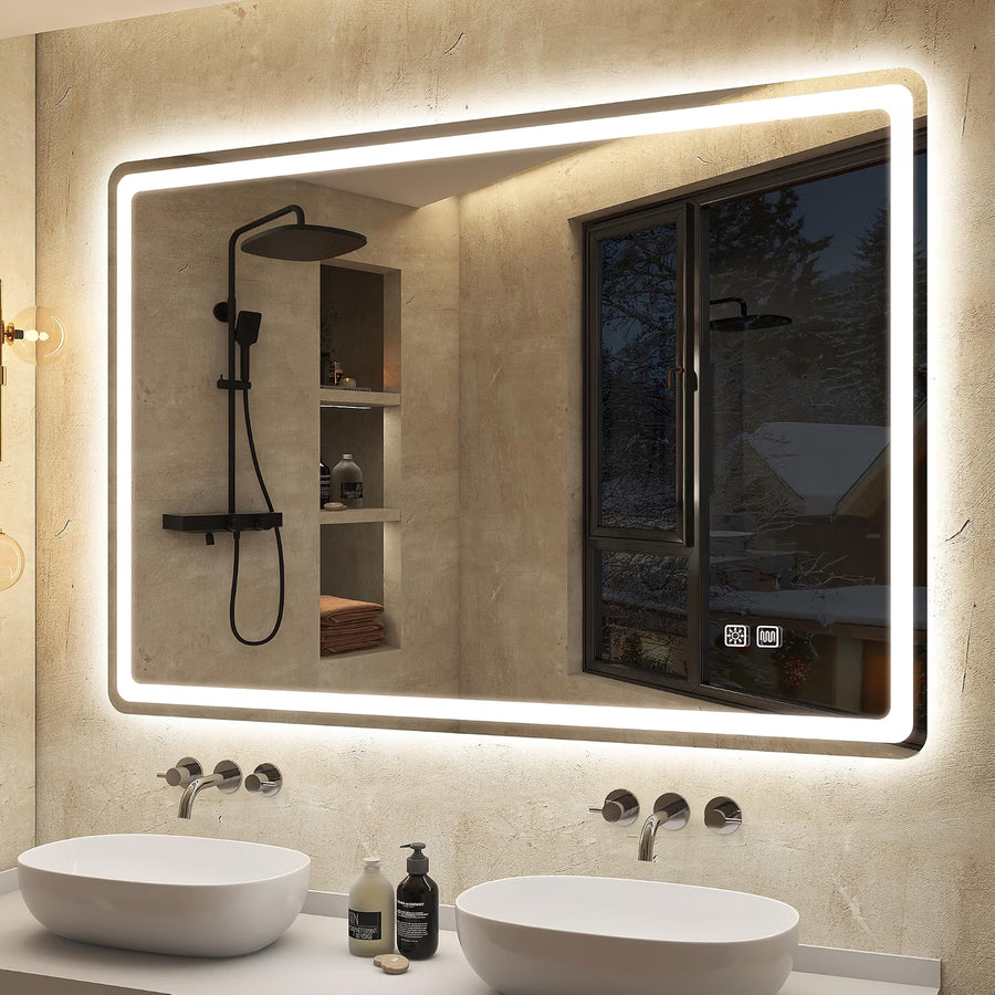 A large rectangular LED-backlit bathroom mirror mounted on a textured beige stone wall above a double-sink vanity. The mirror reflects a black shower fixture and a window view, with two white vessel sinks and chrome faucets below.