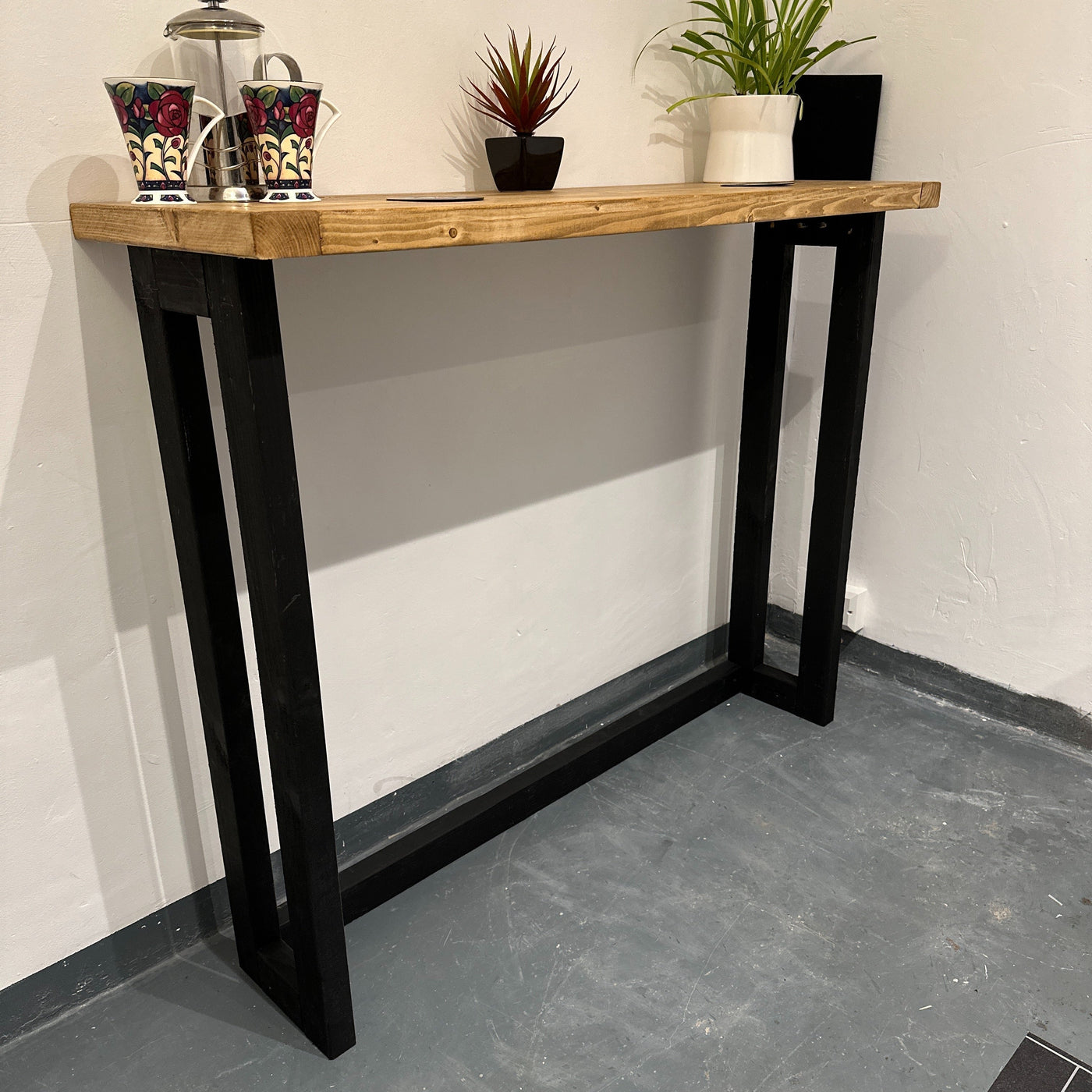 Wooden console table with black legs against a white wall.
