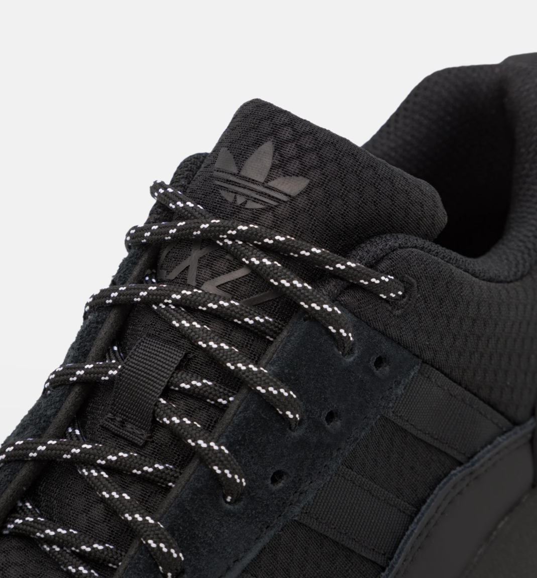 Black Adidas sneaker with white laces on a light gray background