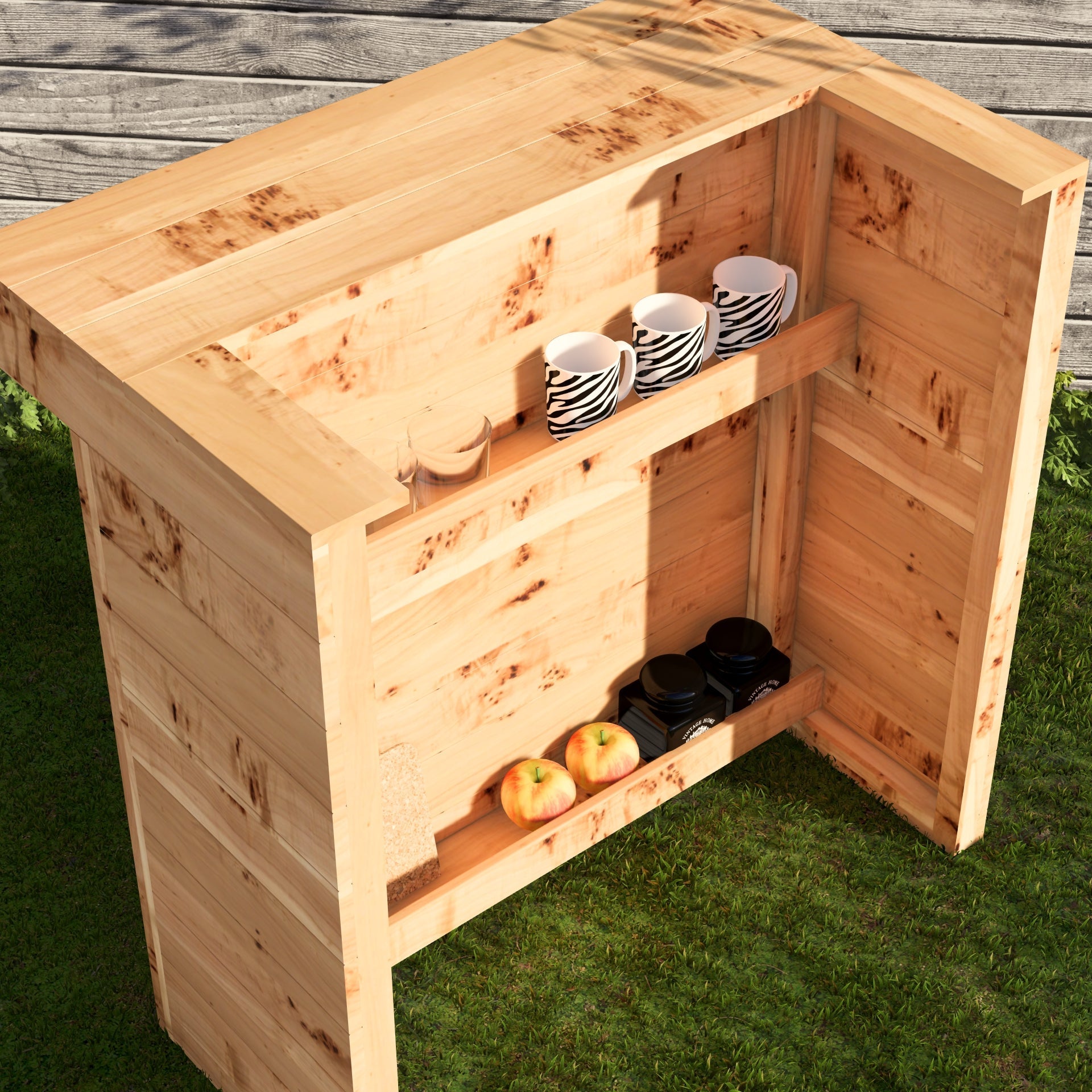Wooden outdoor bar with cups, apples, and bottles on a grassy surface