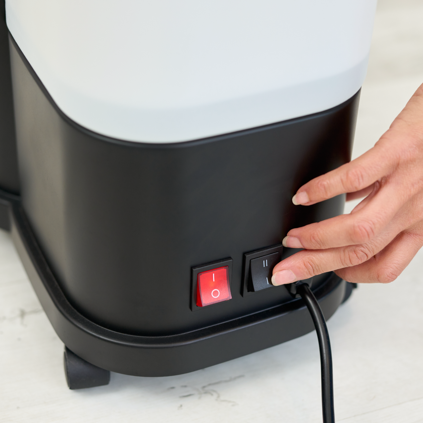 Hand pressing a power switch on a black appliance with a white top.