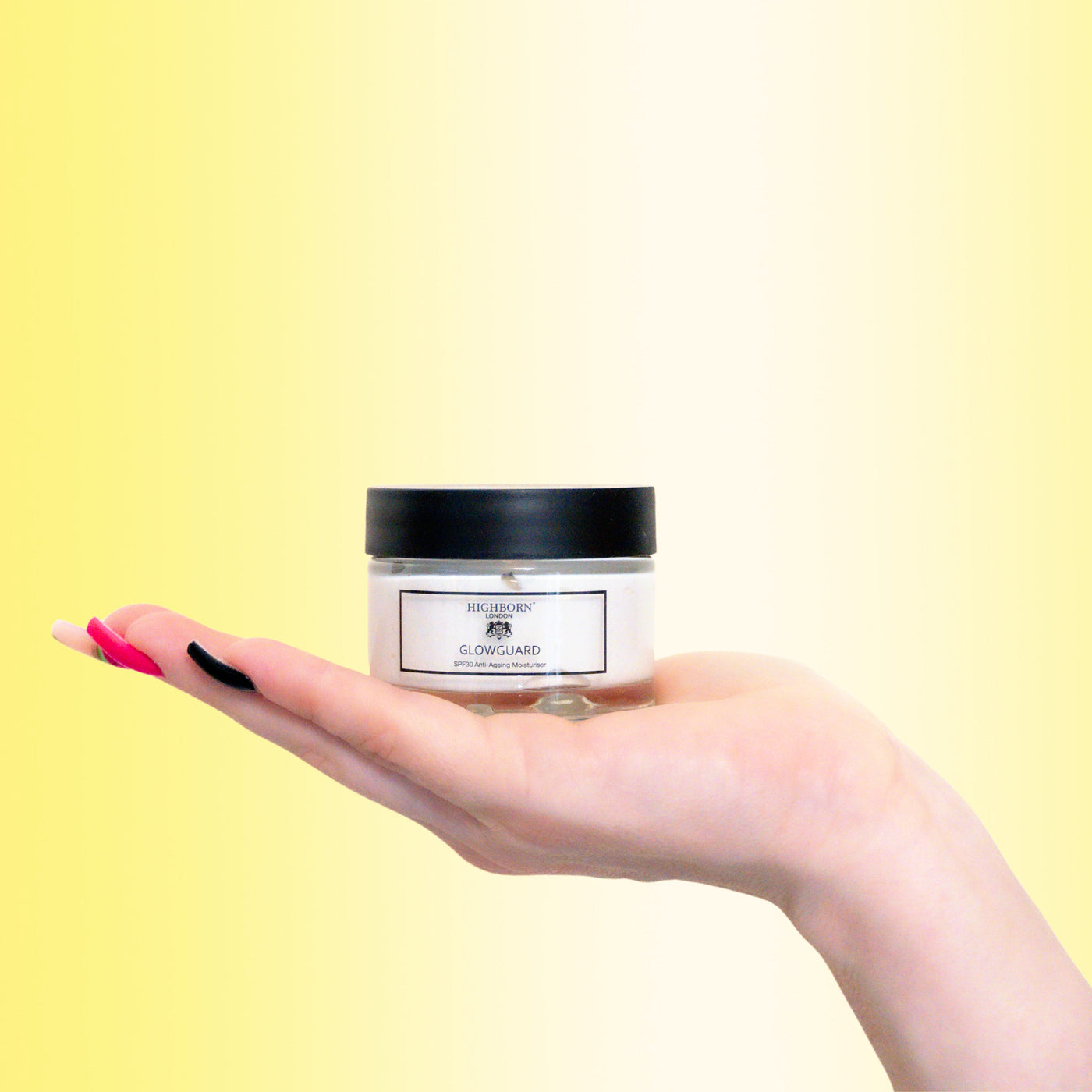 Hand holding a jar of skincare product with a gradient yellow to white background