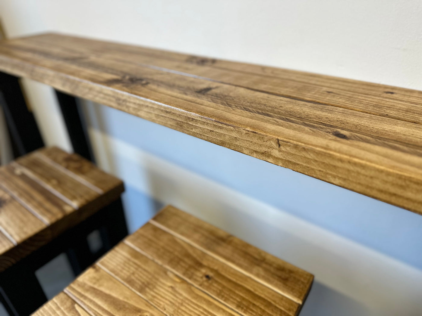 Wooden shelf with two matching wooden stools against a white wall.