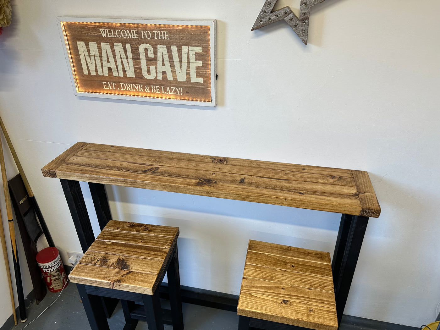 Wooden bar height table with stools underneath, featuring a 'Man Cave' sign on the wall.