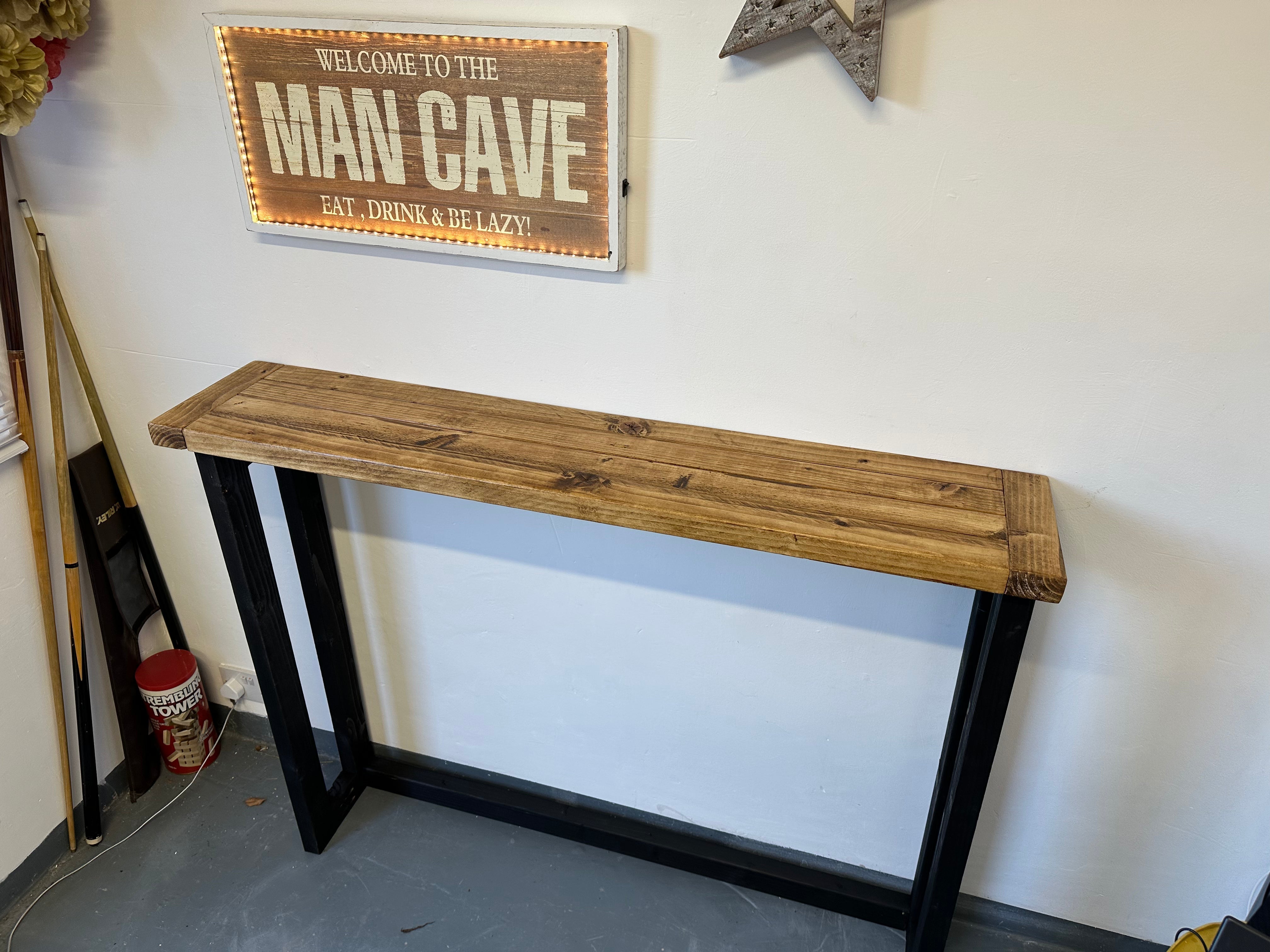 Wooden console table with black metal legs against a white wall with a 'Man Cave' sign.