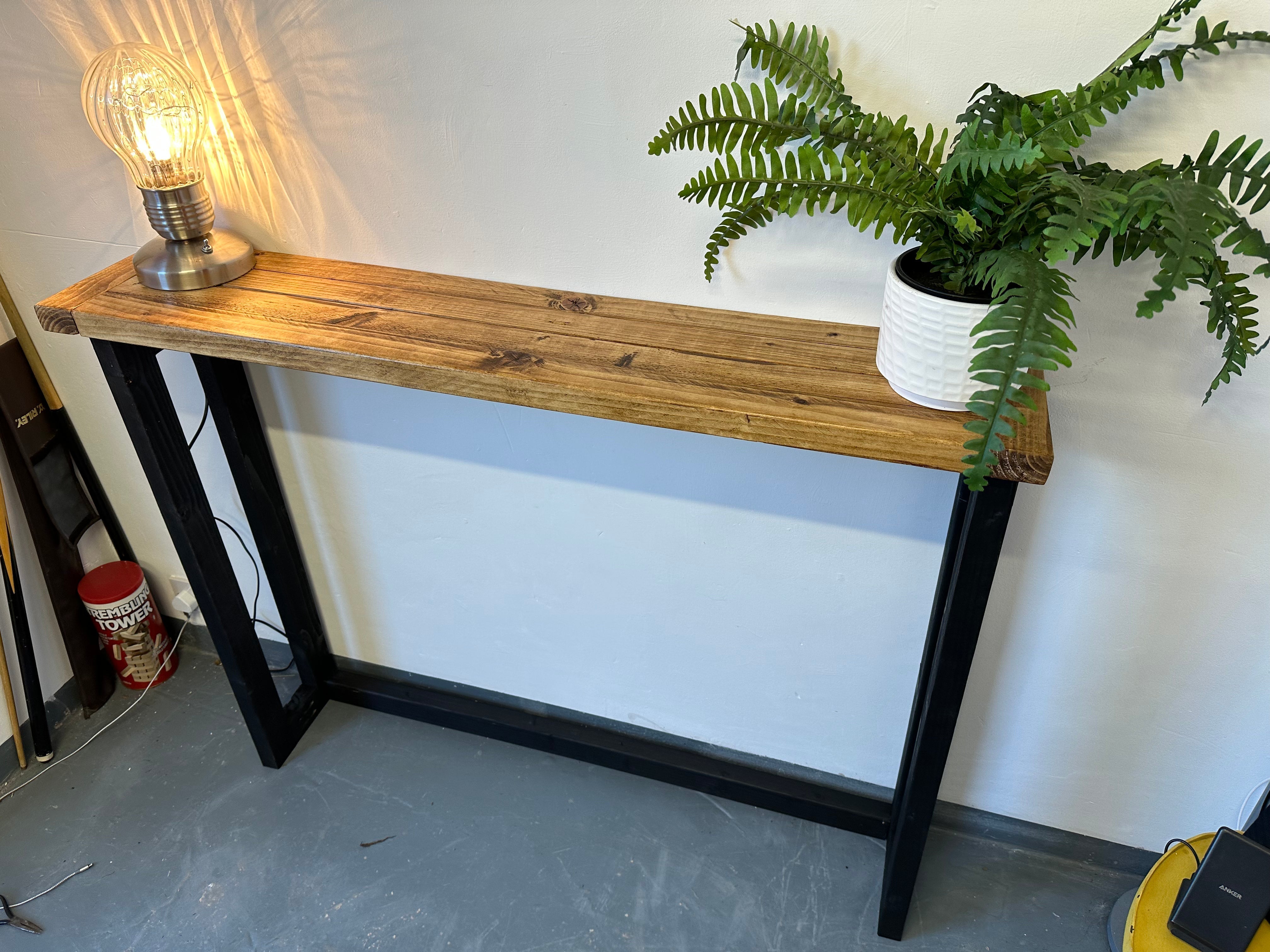 Wooden console table with a lamp and potted plant against a white wall.