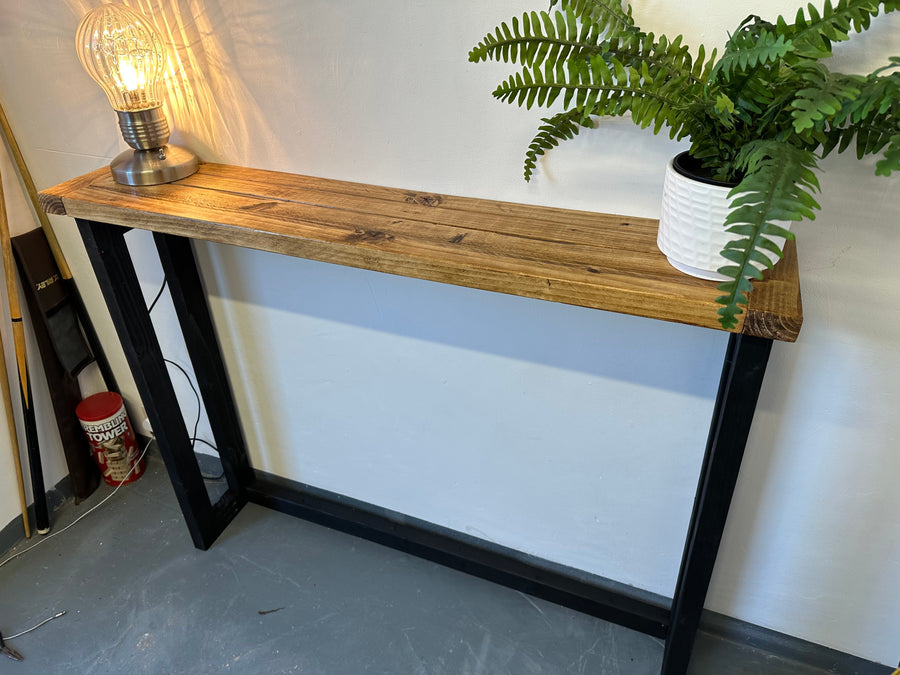 Wooden console table with black metal legs, lamp, and plant against a white wall.