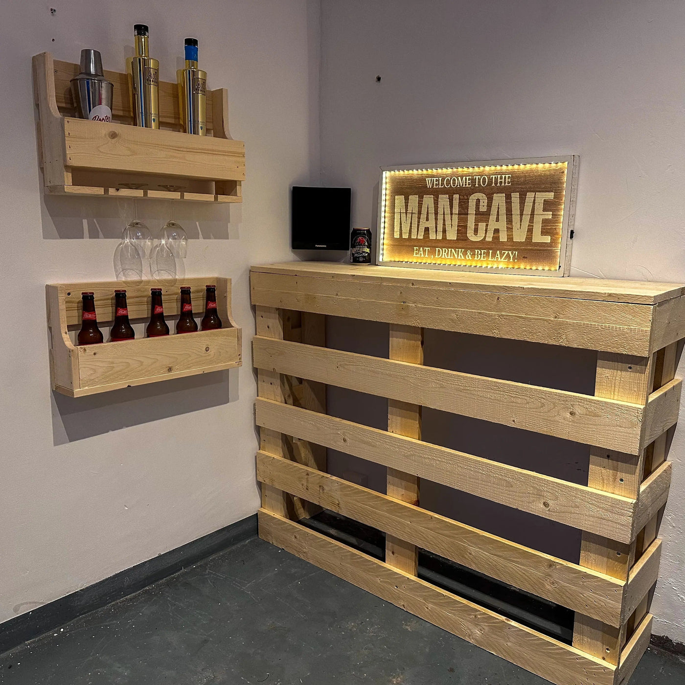 Wooden pallet bar with shelves and a 'Man Cave' sign in a room.