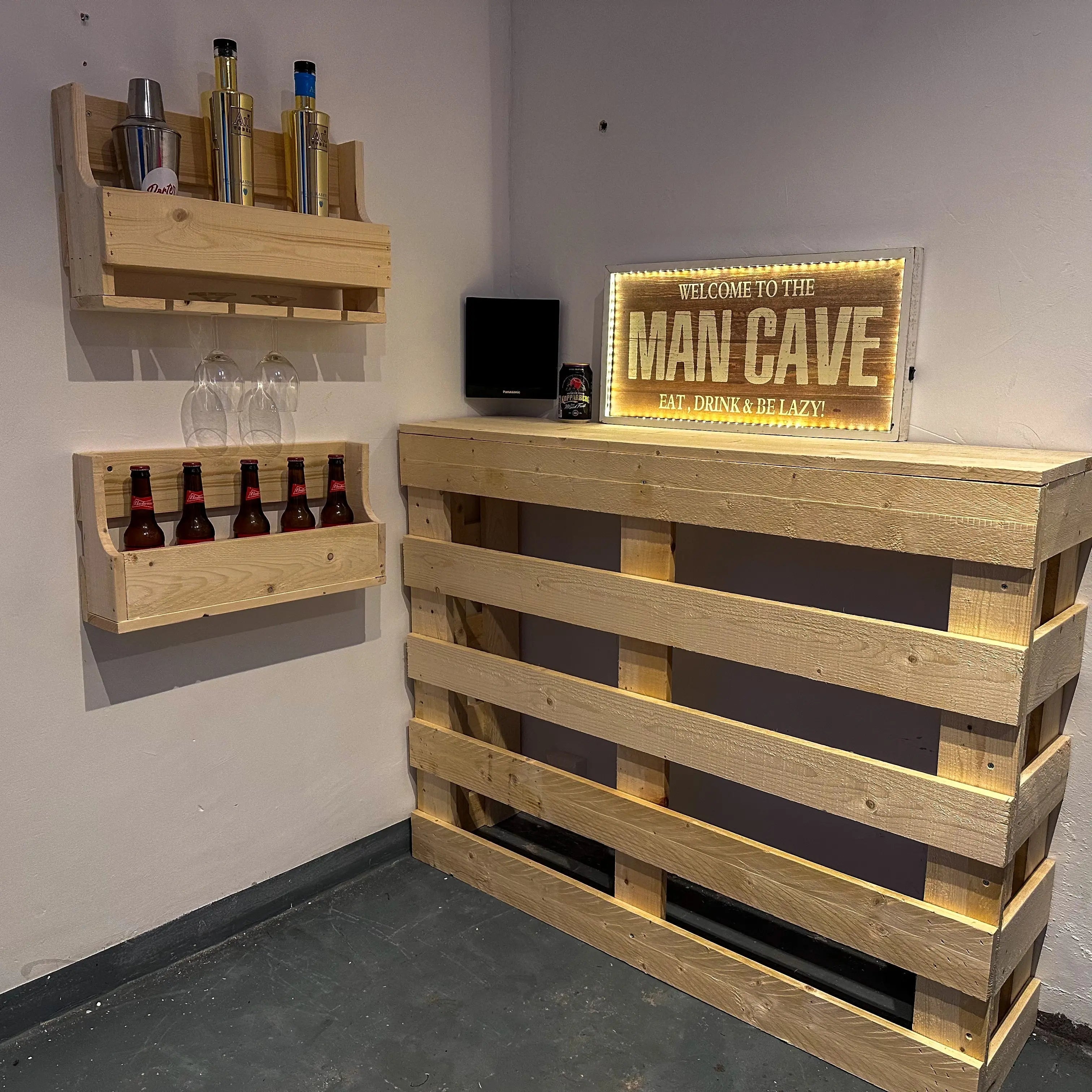 Wooden pallet bar with shelves and a 'Man Cave' sign in a room.