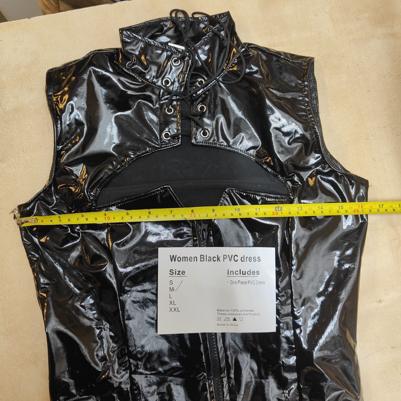 Black PVC dress with a measuring tape and size label on a beige background