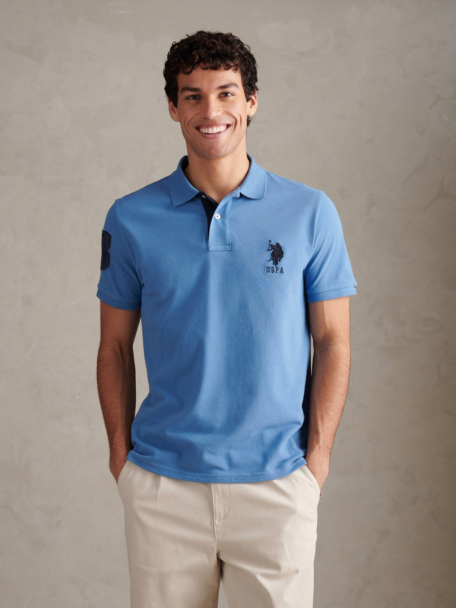 Man wearing a blue polo shirt with a logo on a beige background