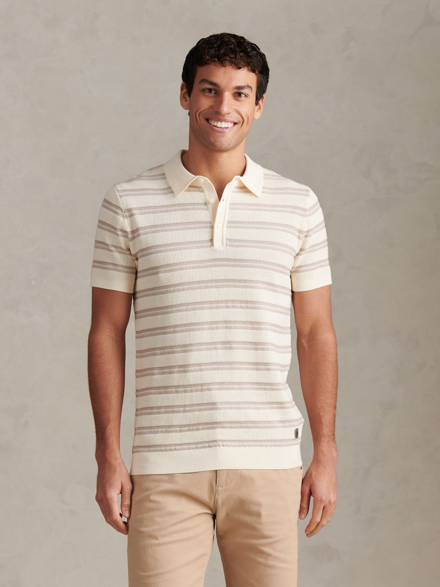 Man wearing a striped polo shirt and beige pants against a plain background