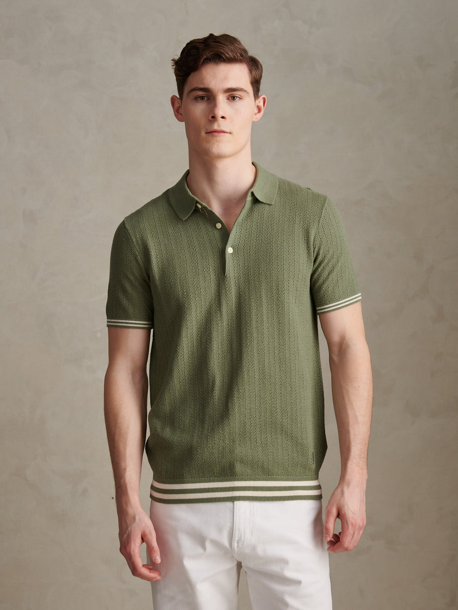 Man wearing a green polo shirt with white pants against a beige background