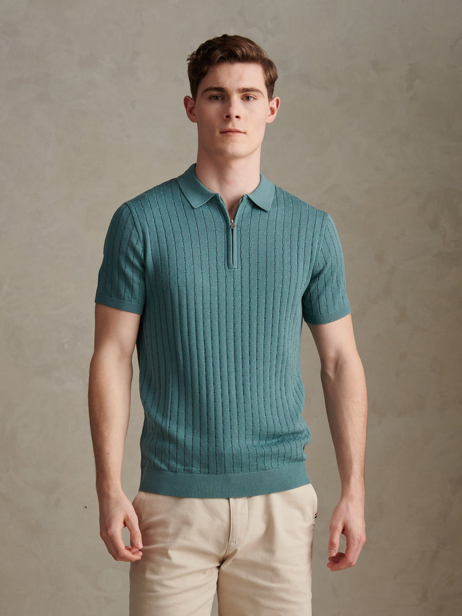 Man wearing a teal ribbed knit polo shirt against a neutral background