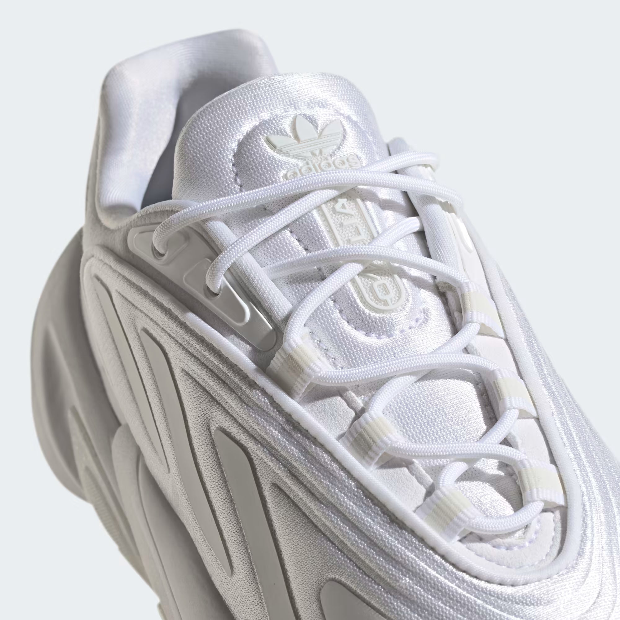 White Adidas sneaker with a light gray sole on a light gray background